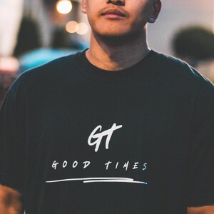 May include: A man wearing a black t-shirt with white text that reads "GT GOOD TIMES" and a white line underneath the text.