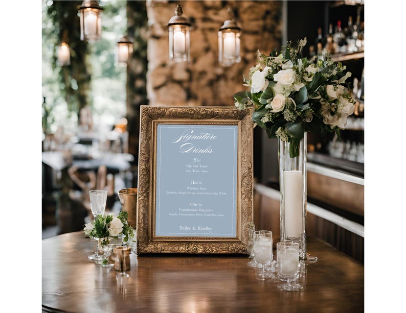 K&ouml;nnte beinhalten: Ein goldfarbener Rahmen mit einem hellblauen Hintergrund und wei&szlig;em Text, der "Signature Drinks" lautet. Das Schild listet eine Vielzahl von Getr&auml;nken mit Namen wie "One and Two", "Here's to", "Cheers" und "Bailey's & Brandy" auf.