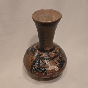 May include: A brown ceramic vase with a narrow neck and a wide base. The vase is decorated with black and white painted designs of birds, plants, and a white rabbit.