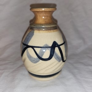 May include: A small, cream-coloured ceramic vase with a brown top and blue and black abstract designs.