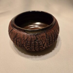 May include: A small, brown ceramic bowl with a textured, tree bark-like exterior. The bowl has a dark brown glaze on the inside.