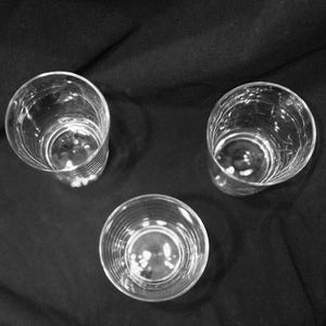 May include: Three clear, empty drinking glasses arranged on a dark surface. The glasses are cylindrical with a slightly textured exterior. The image is a high-angle shot, showcasing the glasses' interiors.