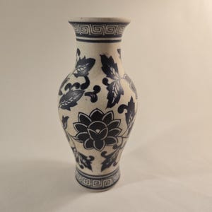 May include: A white ceramic vase with a blue and white floral design. The vase has a narrow neck and a wide base.