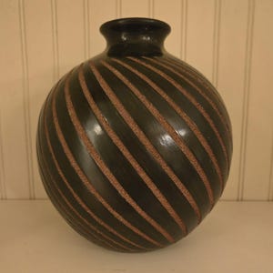 May include: A black ceramic vase with a spiral pattern of brown lines. The vase is round and has a smooth, glossy finish.