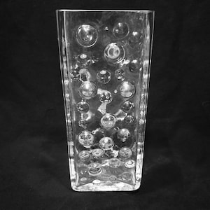 May include: Transparent glass vase, rectangular with a pattern of embedded bubbles. The vase is clear, allowing light to pass through. Suitable for displaying flowers or as a decorative piece.
