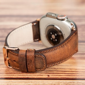 May include: A brown leather watch band with a white stitching detail. The band is designed for a smartwatch with a silver case.