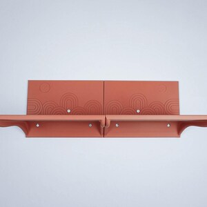 Pode incluir: Prateleira de parede de duas peças na cor terracota com um design de arco decorativo. Cada prateleira tem uma borda frontal curva e é montada com parafusos prateados. As prateleiras são exibidas contra uma parede branca.