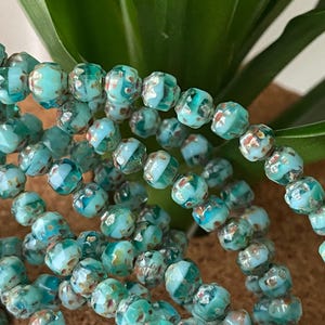 May include: A strand of turquoise blue glass beads with white and gold flecks. The beads are faceted and have a slightly irregular shape.