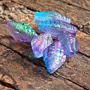 May include: A group of iridescent glass beads in shades of blue, purple, and green. The beads are shaped like seashells and have a textured surface.