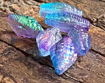 May include: A group of iridescent glass beads in shades of blue, purple, and green. The beads are shaped like seashells and have a textured surface.