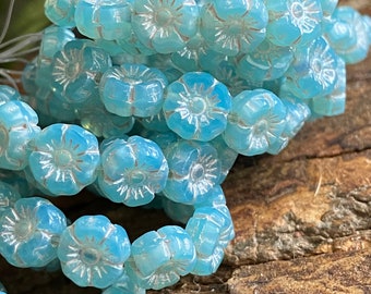 May include: A strand of light blue glass flower beads with a white center. The beads are strung on a clear thread and are arranged in a pile.