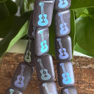 May include: A strand of dark gray guitar-shaped beads with blue and green accents. The beads are strung together on a clear string.