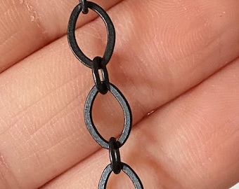 May include: A close-up of a black chain with oval links. The chain is made of metal and has a matte finish.