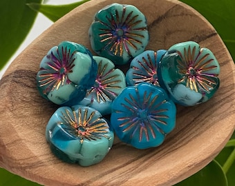 May include: A collection of flower-shaped glass beads in shades of teal and blue, with gold-colored accents. The beads are arranged in a wooden bowl, showcasing their intricate details and vibrant colors. These beads are ideal for jewelry making.