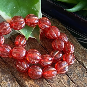 May include: A strand of orange glass beads with a faceted, ribbed texture. The beads are arranged in a circular pattern, suggesting a bracelet or necklace.
