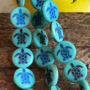 May include: A strand of teal blue wooden beads with a sea turtle design. The turtles are outlined in dark blue and have a textured shell.