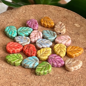 May include: Assortment of colorful leaf-shaped ceramic beads. The beads are in various shades of green, blue, yellow, orange, red, and pink. They are perfect for jewelry making or crafting.