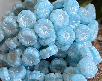 May include: A pile of light blue glass flower beads. The beads are small and have a slightly iridescent finish.