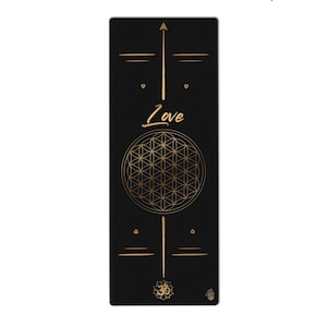 May include: Black yoga mat with gold geometric design and the word "Love". The mat features a central flower of life pattern, with an arrow and lines at the top and bottom. A yoga mat for exercise and meditation.