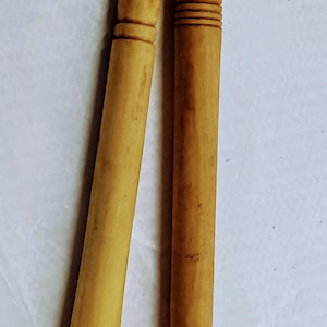 May include: Two wooden sticks with a clay pipe on one end. The sticks are brown and have a natural finish. The pipe is brown and has a small hole in the side.