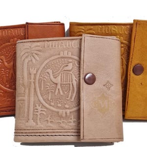 May include: Three leather wallets with embossed designs. The wallets are brown, tan, and beige. The beige wallet has a button closure and the text "MOROCCO" embossed on the front.