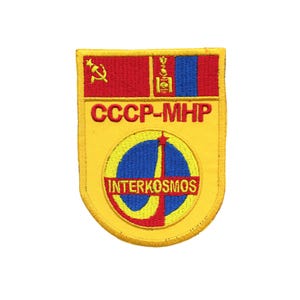 May include: A yellow, red, and blue embroidered patch with the text "CCCP-MHP INTERKOSMOS" and a stylized image of a rocket launching into space.