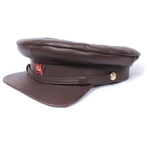 Könnte beinhalten: Eine braune Militärkappe aus Leder mit einem roten Stern und einem goldenen Knopf.