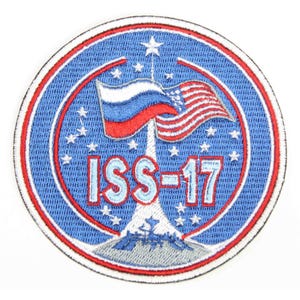May include: A blue and red embroidered patch with the text "ISS-17" in the center. The patch features a rocket launching into space with the American and Russian flags waving in the wind. There are stars surrounding the rocket.