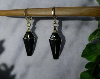 May include: A pair of gold hoop earrings with black coffin-shaped charms. Each charm features a gold cross.