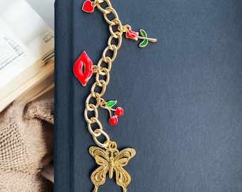 May include: A gold chain bookmark with red and green enamel charms, including a heart, a rose, lips, a cherry, and a butterfly.