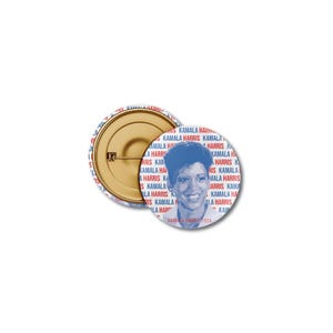 Op de afbeelding: Twee ronde politieke campagnebuttons. Eén button toont een blauw portret van Kamala Harris, met de tekst "KAMALA HARRIS 2024". De andere button toont de pin back. De buttons hebben een witte achtergrond met de woorden "KAMALA HARRIS" in rood en blauw.