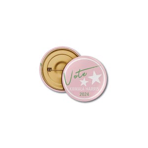 Op de afbeelding: Roze knoop met een witte rand en de tekst "Vote" in groene schrijfletters met twee witte sterren. Onder de tekst staat "Kamala Harris 2024".
