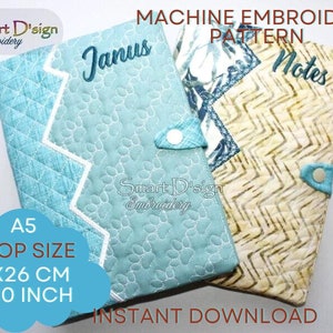 Może przedstawiać: Wzór do haftu maszynowego na okładkę zeszytu z wyszytymi słowami "Janus" i "Notes" na przodzie. Wzór jest przeznaczony do obręczy o rozmiarze 16x26 cm (6x10 cali).