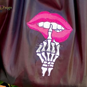 Puede incluir: Diseño bordado de una boca rosa con una mano de esqueleto haciendo el dedo medio.