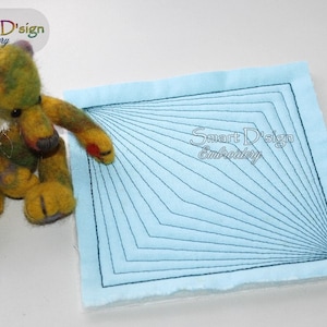 May include: A handmade teddy bear with a green, yellow, and purple color scheme sits next to a light blue square fabric. The fabric features a geometric design of dark blue lines radiating from the corners. The text "Smart D'sign Embroidery" is visible.