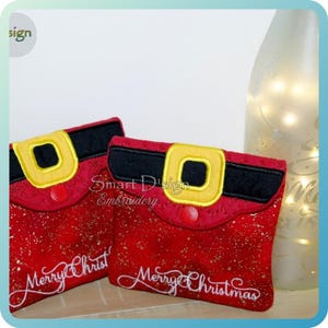 Può includere: Due pochette rosse a tema natalizio con spruzzi d'oro, con design di fibbie nere e gialle. Il testo "Merry Christmas" è ricamato in corsivo bianco su ogni pochette. Pochette festive e decorative.