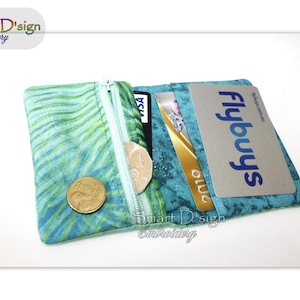 May include: A small, open wallet with a teal and green patterned fabric. The wallet has a zippered coin pouch with a gold coin inside. Credit cards are visible in the open card slots. The text "Flybuys" is visible on one of the cards.
