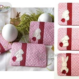 May include: Four pink and red quilted coasters with a white bunny design. The bunnies are embroidered with a red tail and are facing to the left. The coasters are on a white surface.