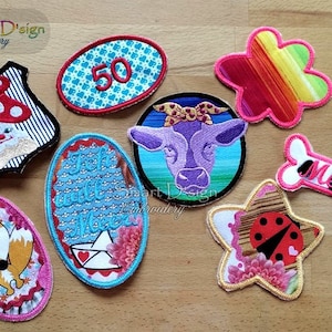 Könnte beinhalten: Eine Sammlung von acht gestickten Bügelbildern mit verschiedenen Designs, darunter ein Pilz, eine Kuh, ein Fuchs, ein Marienkäfer, ein Knochen, eine Blume, ein Boot und die Zahl 50. Die Patches sind alle bunt und haben verschiedene Texturen.