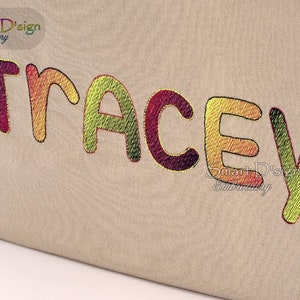 Könnte beinhalten: Der Name "Tracey" ist in einer bunten Farbverlaufschrift auf einem beigefarbenen Stoffgrund gestickt.