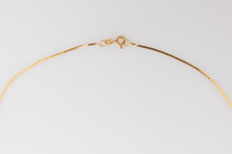 Puede incluir: Un delicado collar de oro con un dise&ntilde;o plano en forma de cadena. El collar presenta un peque&ntilde;o cierre y un anillo de conexi&oacute;n, todo en color oro brillante. El fondo es blanco liso.