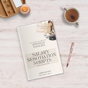 Op de afbeelding: Een crèmekleurig boek met de titel "Salary Negotiation Scripts" met de tekst "The Executive Assistant Success Toolkit". Een pen met een regenboogpatroon, een kopje thee en een kaars liggen ook op het houten oppervlak.