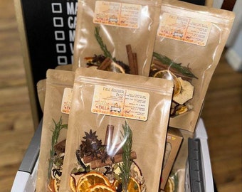 May include: Four brown paper bags filled with dried fruit, spices, and herbs. The bags are labeled "Fall Simmer Pot" and have a small illustration of a house with a chimney. The bags are in a white wicker basket.
