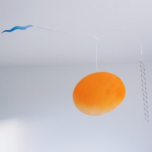 A hanging piece, you can see thin blue cloud in the left, in the middle a vivid orange sun, and a thin black ladder on the right. They are balanced on a thin white wires. There is a white wall behind the piece.