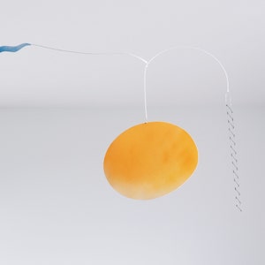 A hanging piece, you can see thin blue cloud in the left, in the middle a vivid orange sun, and a thin black ladder on the right. They are balanced on a thin white wires. There is a white wall and ceiling behind the piece.
