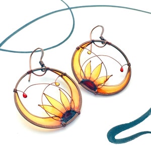 Two circle-shaped earrings in dark copper, each earring contains a half sunflower made with wire and colored in yellow, amber and brown transparent colors.