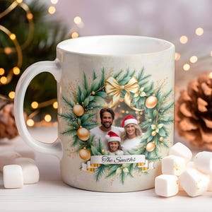 Puede incluir: Taza de cerámica blanca con un diseño de corona navideña que presenta una foto familiar. La corona incluye adornos dorados, un lazo y follaje. La foto familiar muestra a un hombre, una mujer y un niño con gorros de Papá Noel. El texto "The Smiths" está en una pancarta.