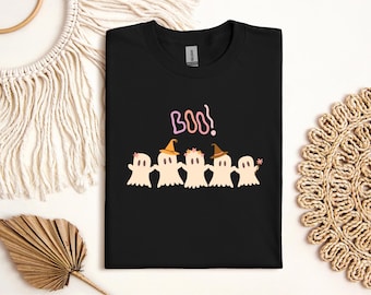 May include: Black t-shirt featuring a Halloween design. The shirt displays the word "Boo!" in pink and a row of cartoon ghosts wearing hats and holding a wand. The ghosts are in shades of beige and orange.