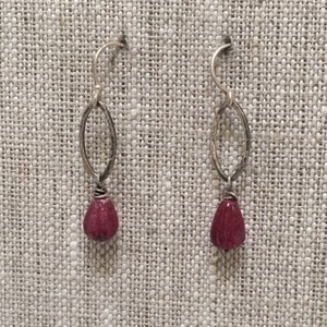 May include: A pair of silver earrings with a teardrop-shaped, deep red gemstone hanging from each.