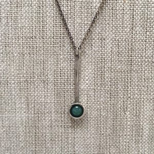 May include: A silver necklace with a long, thin pendant and a round, teal-coloured stone.